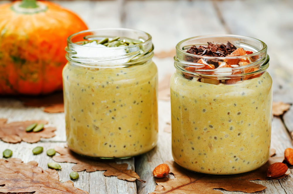 Pumpkin Spice Overnight Oats in glass jars topped with pumpkin seeds and nuts, set on a rustic wooden table with autumn leaves and a fresh pumpkin in the background.