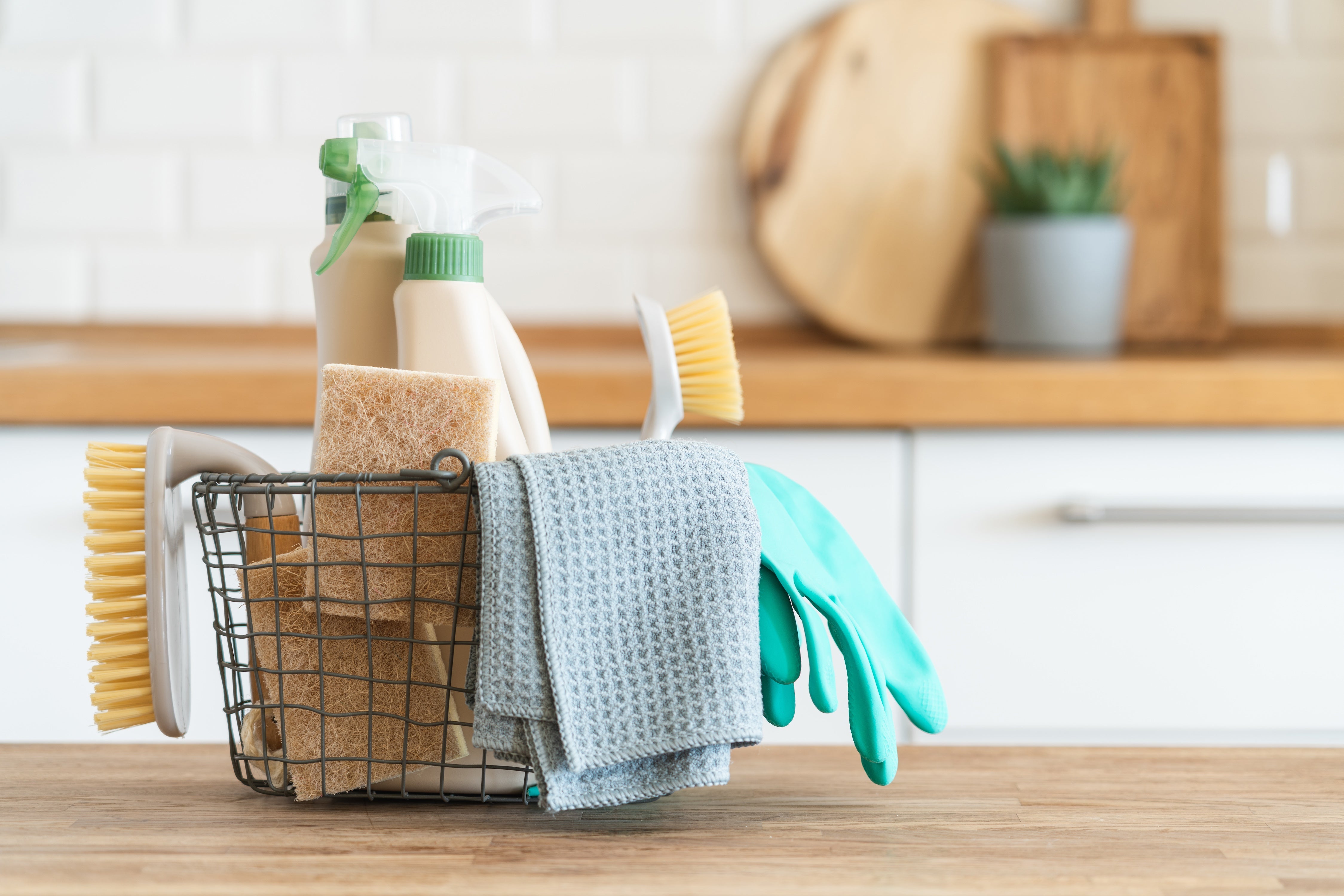 A wire basket full of cleaning supplies on a butcher block countertop