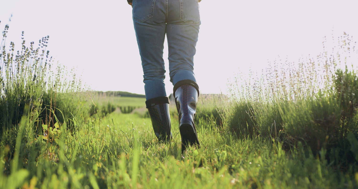 woman lower body pictured,  wearing jeans and rubber boots, walking through a green field
