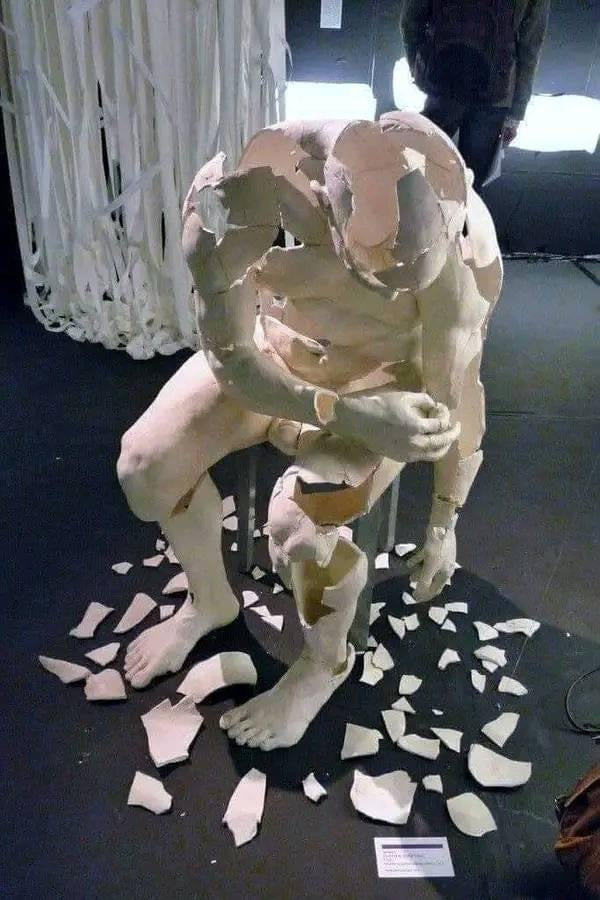 Artistic sculpture of a fragmented human figure sitting with head bowed, made of broken ceramic pieces, symbolizing emotional struggle, vulnerability, and the journey of healing and rebuilding.