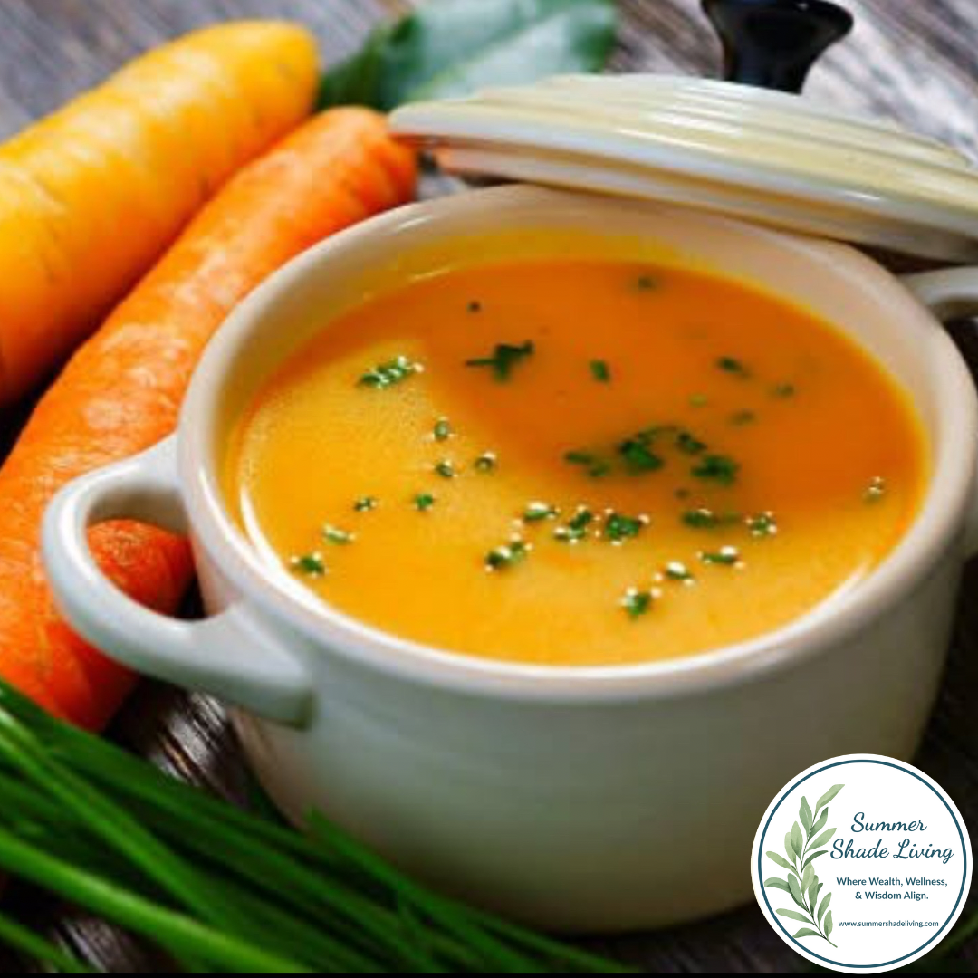 Creamy carrot ginger detox soup served in a white ceramic bowl, garnished with fresh herbs, surrounded by raw carrots and chives, with the Summer Shade Living logo in the corner.