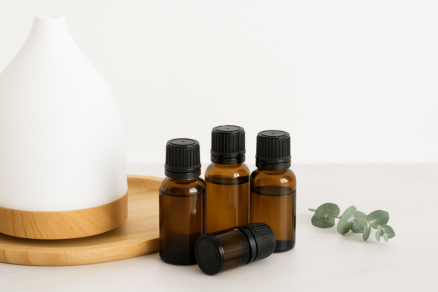 White background with 4 brown glass essential oil bottles, a green eucalyptus spring, and a white diffuser, 