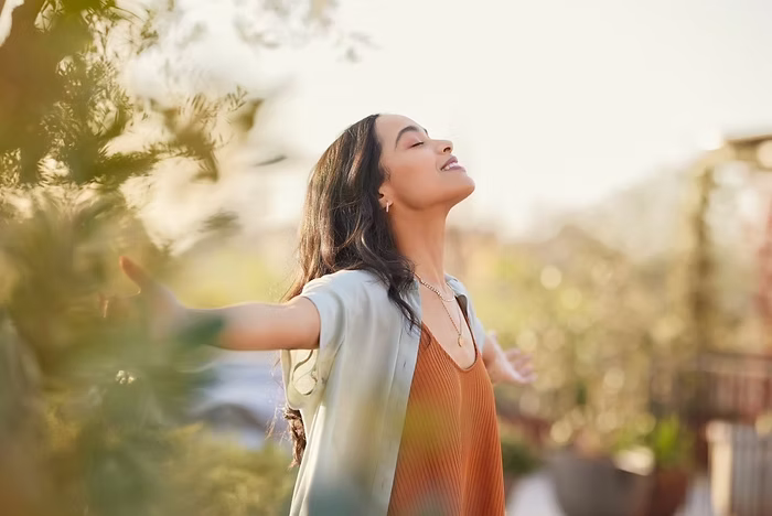 A peaceful woman outdoors with arms open and eyes closed, embracing sunlight and calm energy, symbolizing freedom, mindfulness, and emotional wellness—featuring the Summer Shade Living logo in the corner.