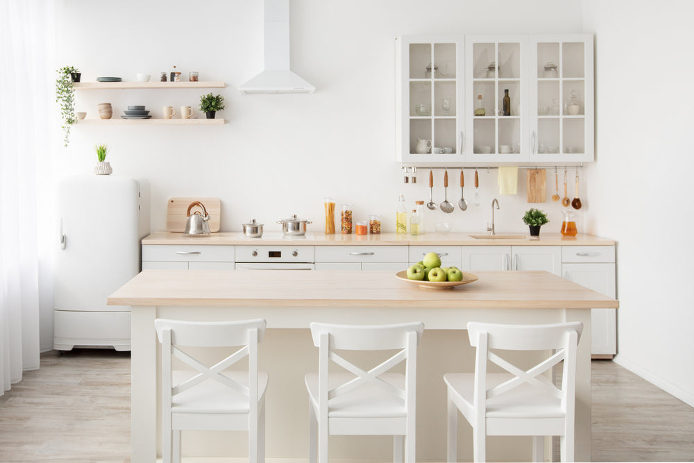 Bright modern white kitchen with natural wood accents, non-toxic cookware, and fresh green apples on the counter for toxin-free living on a budget.