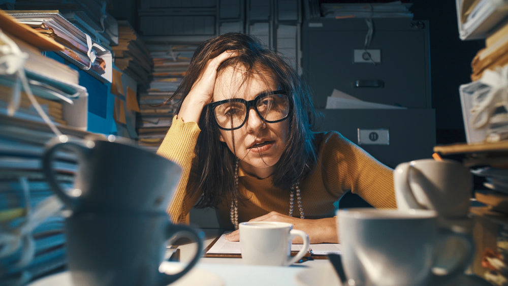 Exhausted woman overwhelmed by paperwork and stress, symbolizing the effects of cortisol imbalance and chronic fatigue