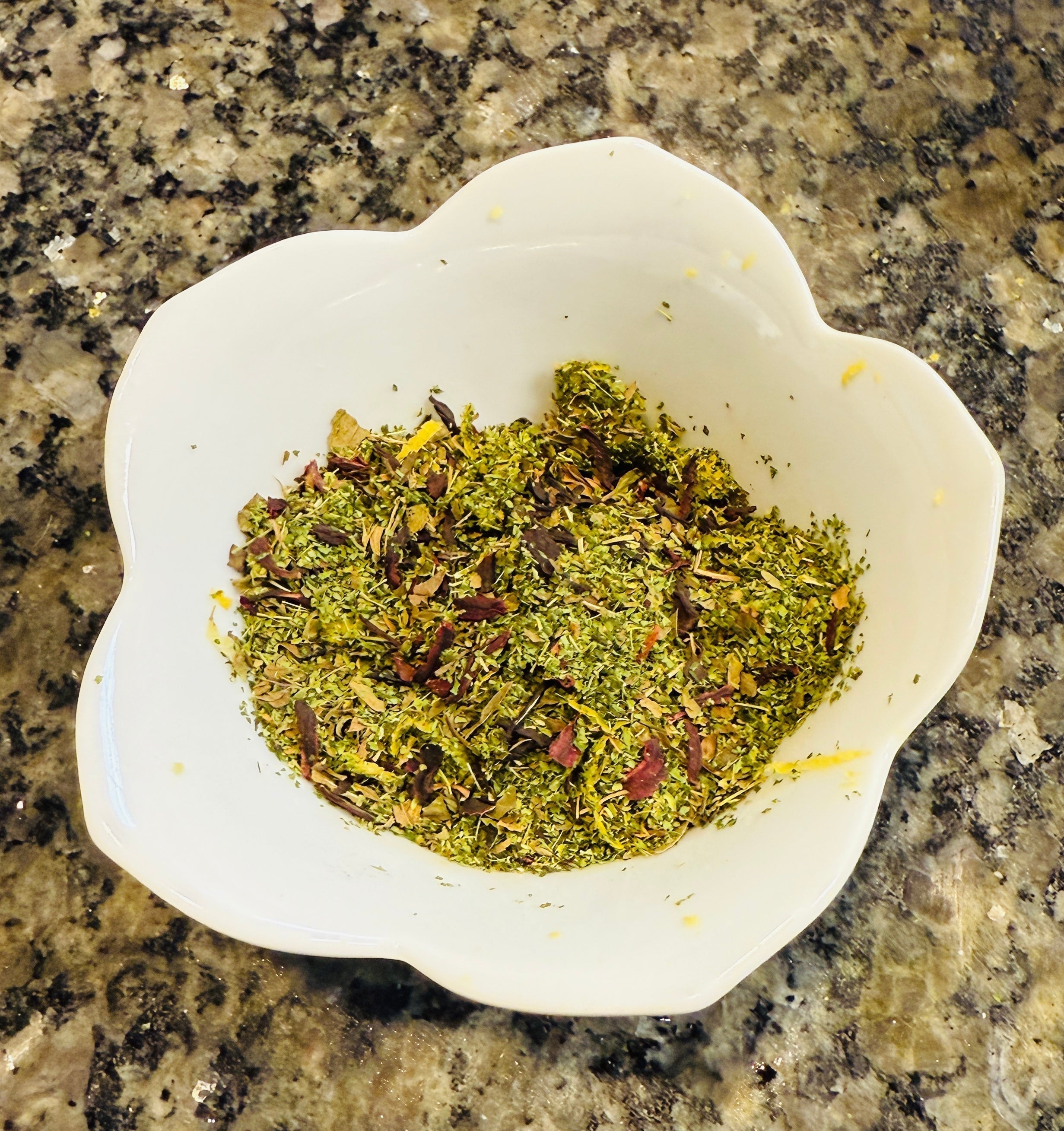 Handcrafted loose leaf herbal tea blend for Summer Shade Sippin’ Wellness Tea, featuring dried moringa, peppermint, hibiscus, chamomile, and lemon zest in a white floral-shaped bowl on a granite countertop.